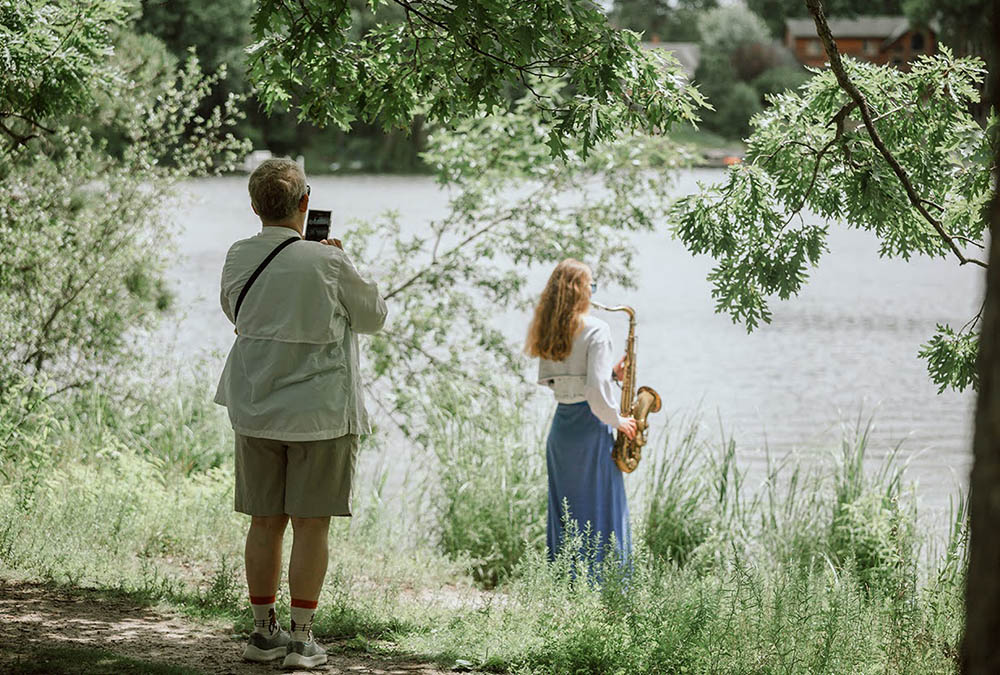 Everest collaborated with a variety of musicians to create the Sound Garden, an immersive music experience in a beautiful outdoor space. (Photo by Tamar Serin) Woman plays saxophone at the shore of Silverwood Lake while another woman takes a photo of her.
