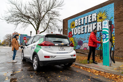 Two people with an electric vehicle at a charging station.