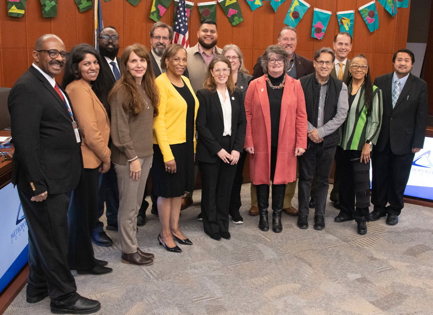 16 people posing in three rows in the Council chambers.
