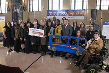 Two rows of about a dozen people each standing or sitting in chairs in the concourse at Union Depot.